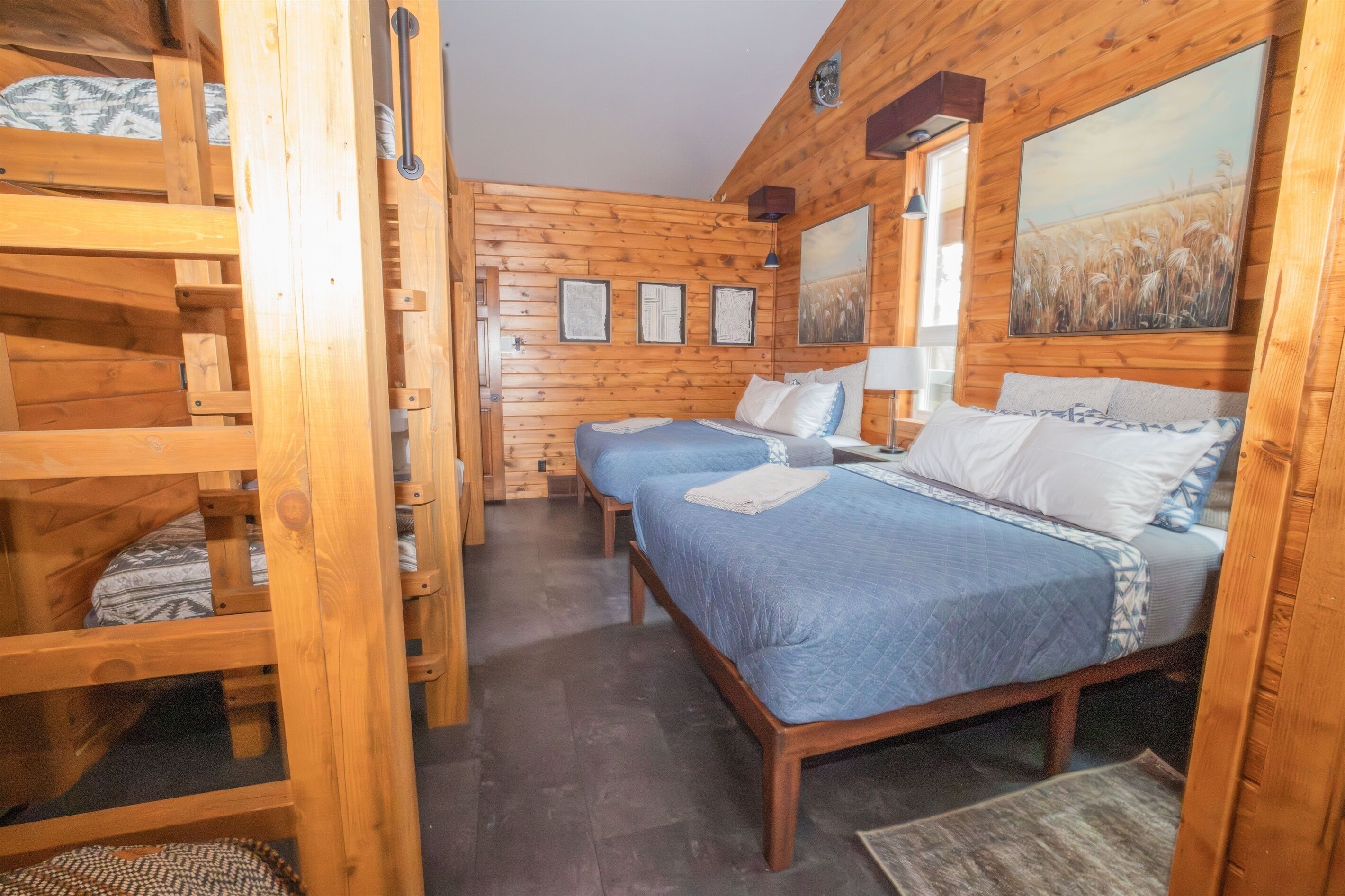 Una habitación de cabaña de madera con literas, una cama grande y un cuadro en la pared.