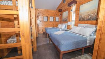 Una habitación de cabaña de madera con literas, una cama grande y un cuadro en la pared.