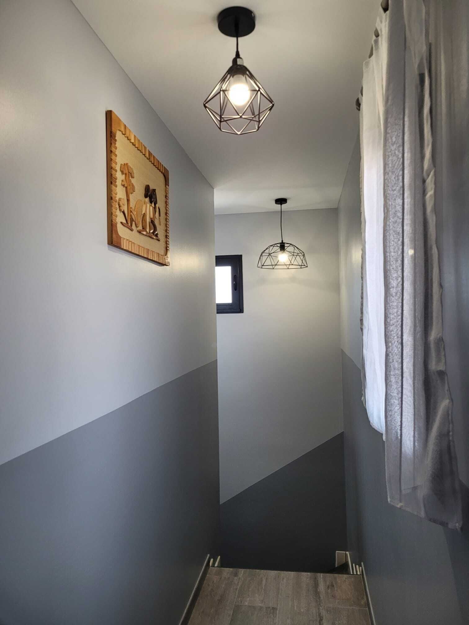 A narrow hallway with a wooden floor, a geometric light fixture, and a framed picture on the wall.
