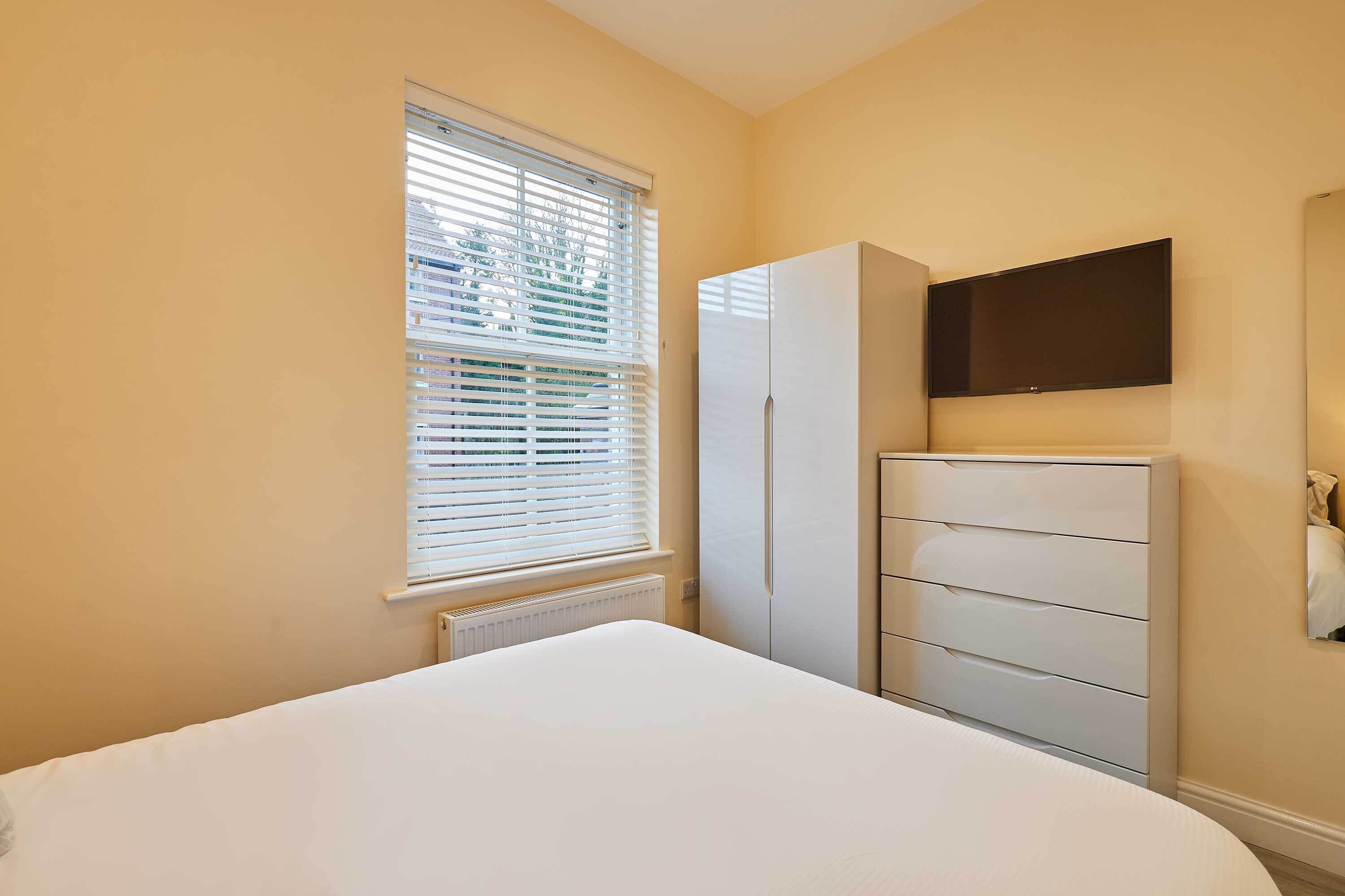 A bedroom with a bed, a wardrobe, a radiator, and a TV mounted on the wall.