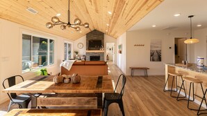 Un'ampia cucina con pavimento in legno, un'isola centrale con sgabelli, un'area pranzo con tavolo e sedie in legno e un angolo salotto accogliente con divano e camino.