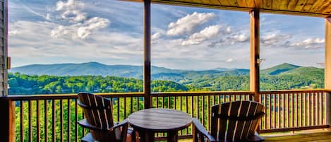 A covered outdoor seating area with a table and chairs, overlooking a mountainous landscape.