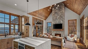A spacious kitchen with a large island, wooden cabinets, and a stone fireplace. - Clouds in My Coffee at Eagles Nest- walk to Village amenities, view, hot tub, golden tee arcade (Banner Elk)