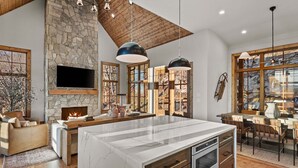 A spacious kitchen with a large island, stone fireplace, and wooden accents. - Clouds in My Coffee at Eagles Nest- walk to Village amenities, view, hot tub, golden tee arcade (Banner Elk)
