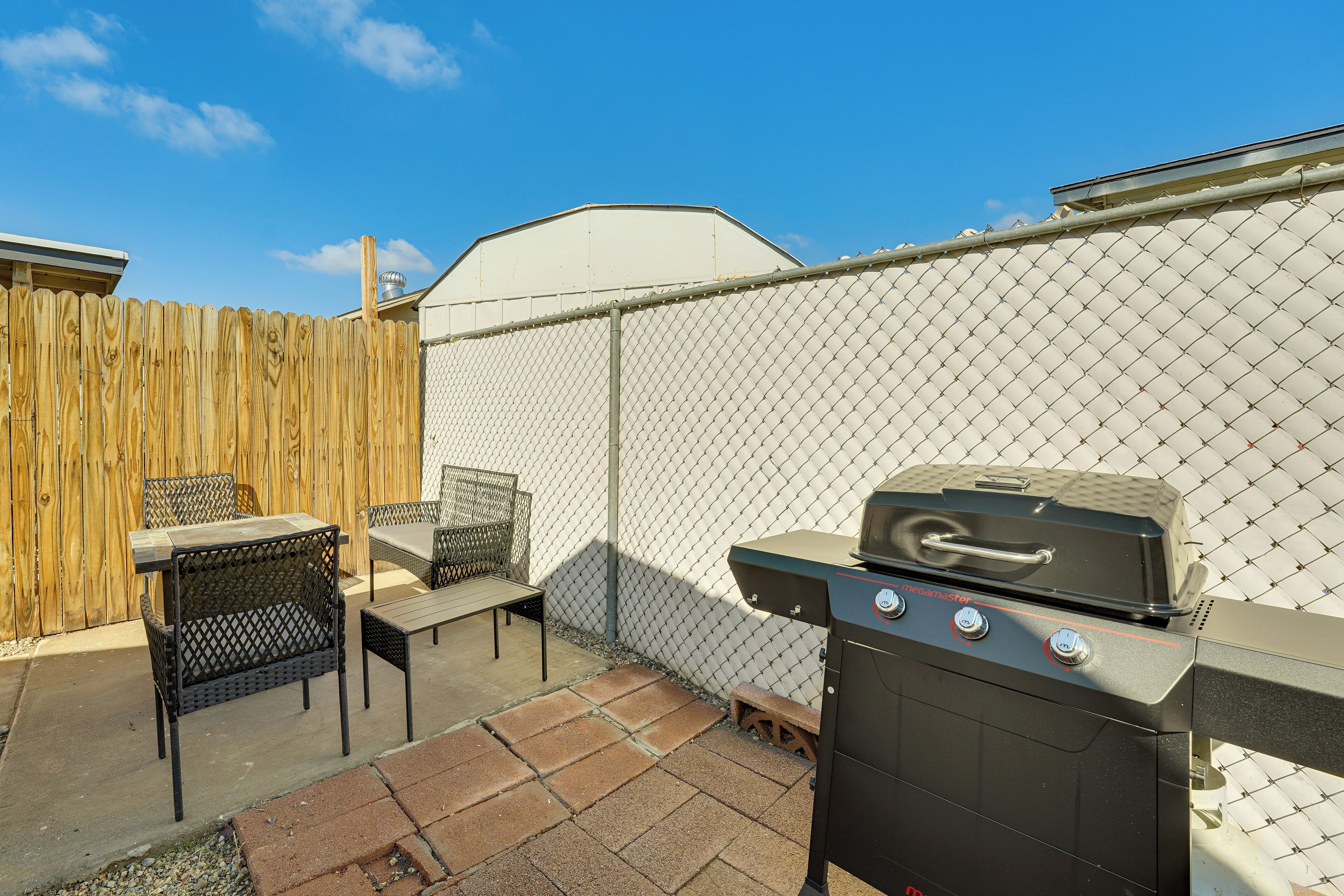 Un patio trasero con cerco de madera, una parrilla y mobiliario exterior.