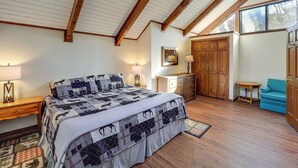 Quarto com cama grande, vigas de madeira no teto, cômoda, cadeira azul e guarda-roupa.