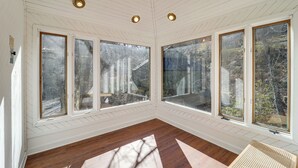 Quarto com grandes janelas, piso de madeira e teto com iluminação embutida.