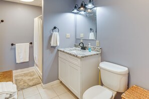 Une salle de bain avec des toilettes blanches, un lavabo doté d’un plan de travail en marbre, un miroir au-dessus du lavabo et un rideau de douche.