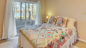 Una camera da letto con un letto grande, una finestra con tende e vista su alberi e un lago.
