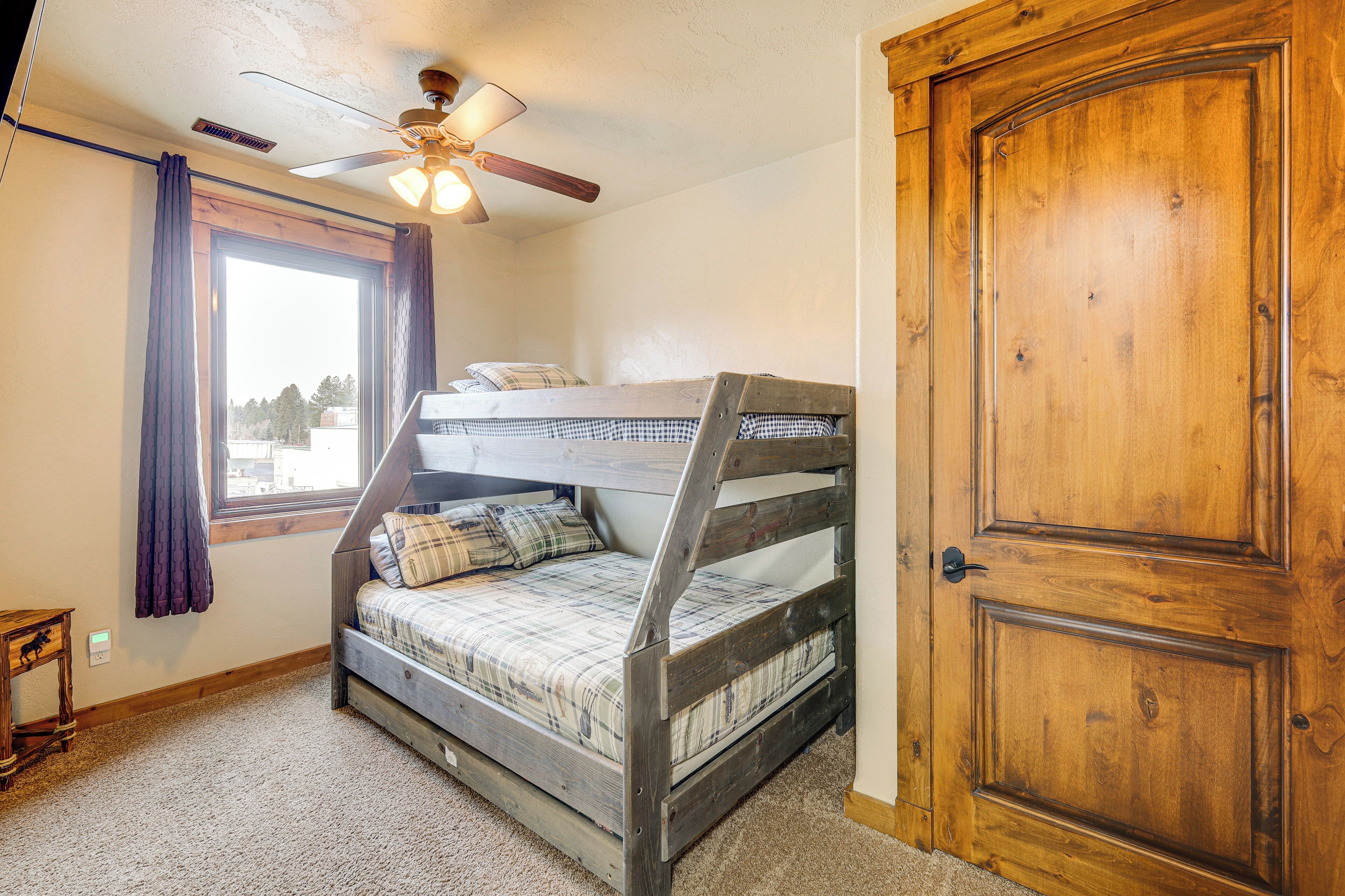 A bunk bed room with a ceiling fan, a window with curtains, and a wooden door.