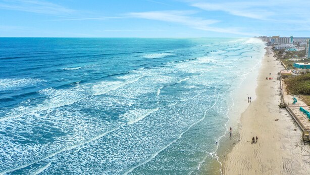 Une plage avec des vagues, un rivage sablonneux et des bâtiments le long de la côte.