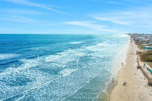 A beach with waves, a sandy shore, and buildings along the coastline. - Relaxed Oceanview Condo with Pool, Balcony & Steps to the Sand (New Smyrna Beach)