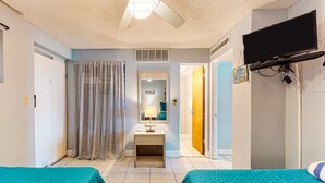 A hotel room with two beds, a ceiling fan, a television mounted on the wall, and a mirror above the dresser. - Private Balcony, Oceanfront Pool, Walk to Boardwalk & Pier (Daytona Beach)