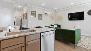 A modern kitchen with a built-in dishwasher, a green sofa, and a flat-screen TV mounted on the wall.