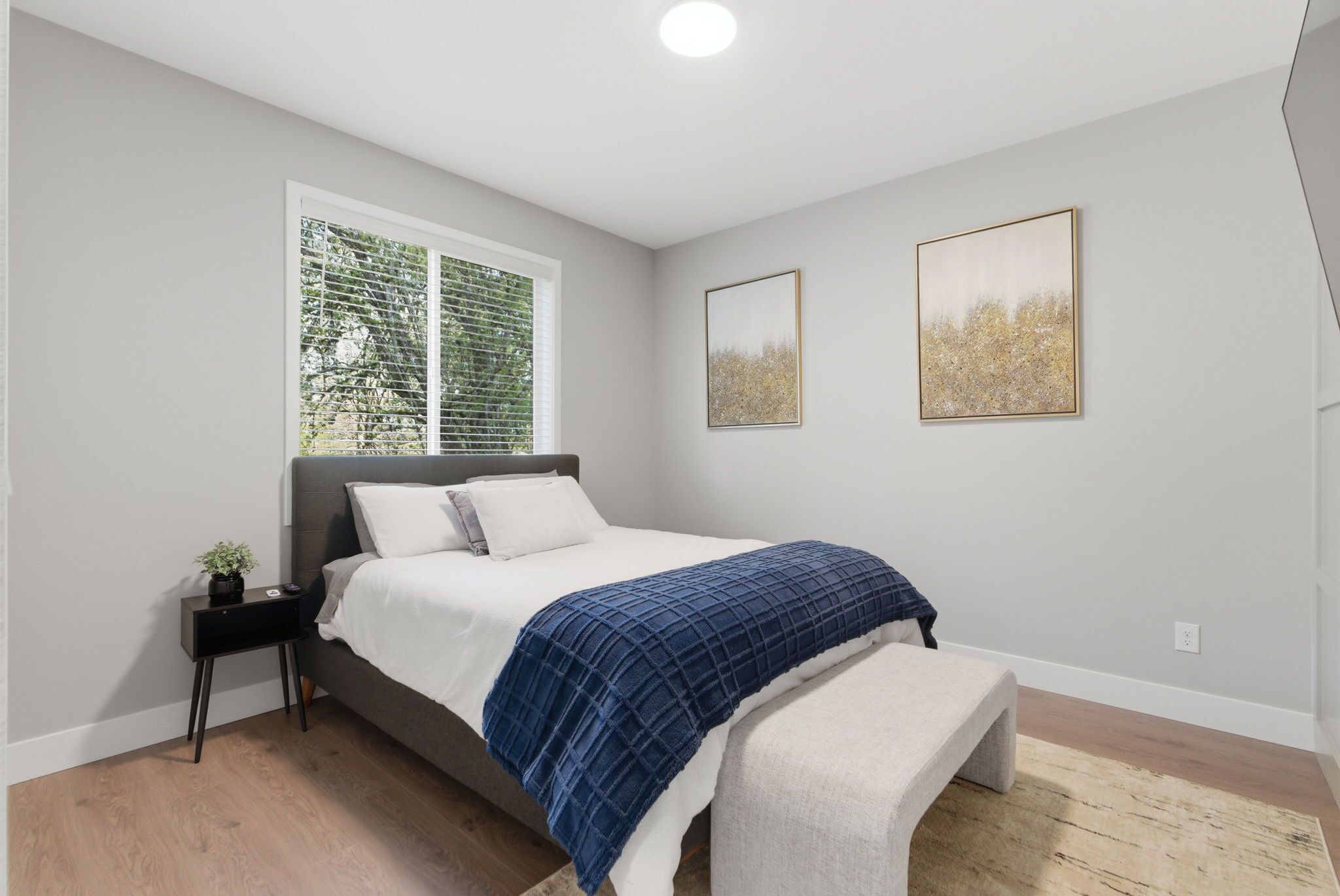 A bedroom with a bed, bedside table, window, and two wall-mounted paintings.