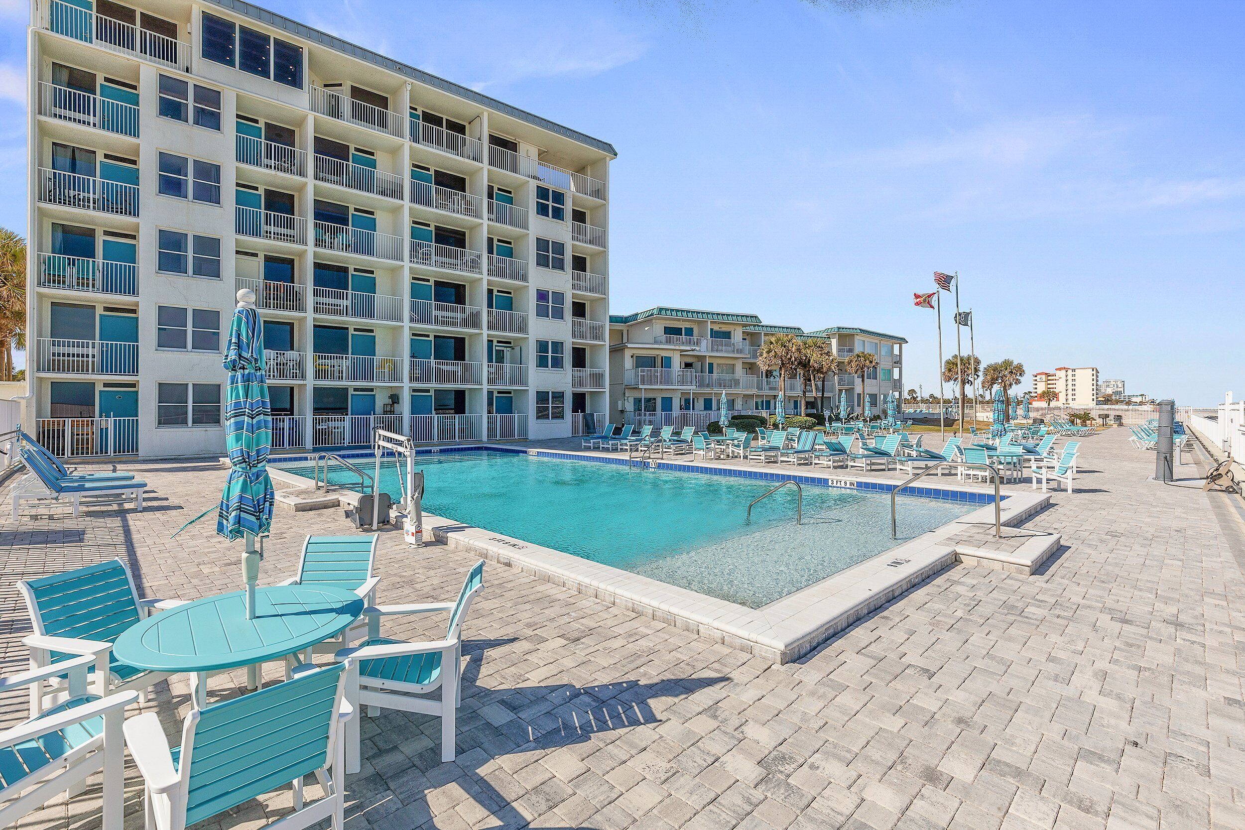 A hotel with a swimming pool, lounge chairs, and a view of the ocean.