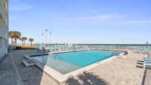 Una piscina rettangolare con bordo piastrellato, circondata da sedie a sdraio e un corrimano.