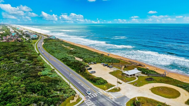 Vista aerea di una zona costiera con una strada, una spiaggia e degli edifici.