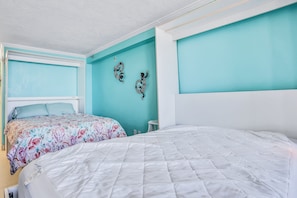Ein Schlafzimmer mit einem großen Bett, einem kleineren Bett, türkisfarbenen Wänden und Wanddekorationen.