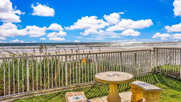 A balcony with a view of the beach and ocean, featuring a round table and a small bench. - Ground Floor Oceanfront Condo with Pools & Easy Beach Access (Daytona Beach)