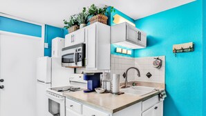 A compact kitchen with white cabinets, a microwave, a coffee maker, and a sink. - Ground Floor Oceanfront Condo with Pools & Easy Beach Access (Daytona Beach)