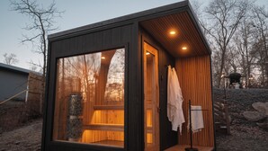 A small, modern cabin with a large window, a wooden door, and a bench outside. - Family-Friendly Cabin with Hot Tub, Sauna, Firepit with Loft, Sleeps 12 (Crosslake)