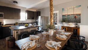 A modern kitchen with dark cabinets, a wooden island, and a dining area set for a meal. - Family-Friendly Cabin with Hot Tub, Sauna, Firepit with Loft, Sleeps 12 (Crosslake)