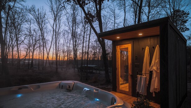 A hot tub with a wooden deck, a small wooden cabin with a door, and towels hanging on a rack. - Family-Friendly Cabin with Hot Tub, Sauna, Firepit with Loft, Sleeps 12 (Crosslake)