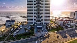 A tall hotel with a central entrance, parking lot, and ocean view. - Oceanfront Corner Condo w/ Balcony, Pool, & Rocket Launch Views (Daytona Beach)