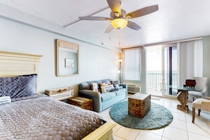 Ein Hotelzimmer mit einem Bett, einem Schlafsofa, einem Couchtisch, einem Sessel, einem Deckenventilator und einem großen Fenster.