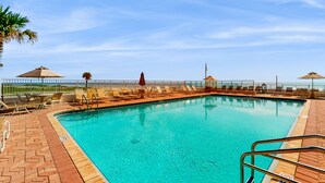 Ein Schwimmbecken mit Liegestühlen und Sonnenschirmen, umgeben von einer Ziegelterrasse und einem Zaun.