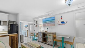 Een moderne keuken met een zwarte koelkast, een houten kast en een eethoek met blauwgroene stoelen en een witte tafel.