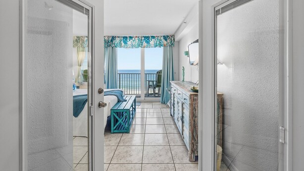 Een kamer met balkon, een bed, bureau en dressoir.