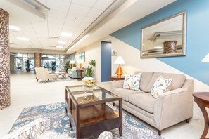 A modern lobby with a glass coffee table, a beige sofa, and a blue accent wall. - Oceanfront 12th-Floor Suite with Views, Pool & Prime Location (Daytona Beach)