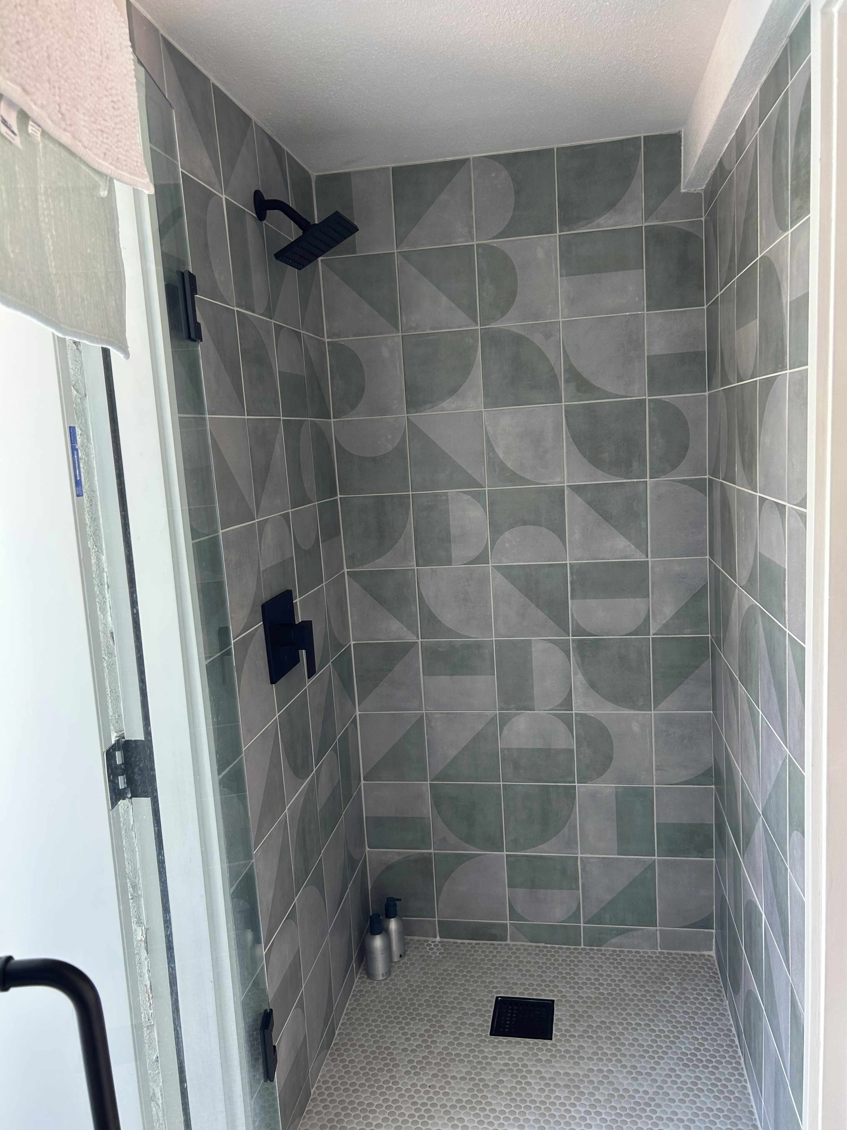 Ein Duschbereich mit geometrischem Fliesenmuster, einer Handbrause und einem Ablauf.