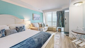 Hotellihuone, jossa on sänky, sohva, ruokapöytä ja ikkuna, jossa on verhot.