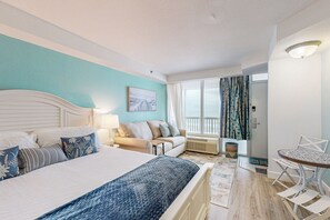 Ein Hotelzimmer mit Bett, einer Couch, einem Esstisch und einem Fenster mit Vorhängen.