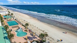 A beach resort with a swimming pool, lounge chairs, and a view of the ocean. - Oceanfront Studio w/ Balcony & Resort Perks Near Boardwalk (Daytona Beach)