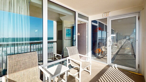 A balcony with a view of the ocean, a chair, a small table, and an exit sign. - Oceanfront Studio w/ Balcony & Resort Perks Near Boardwalk (Daytona Beach)