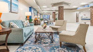 Un hall d’hôtel avec un canapé bleu, des fauteuils beiges, une table basse ornée de fleurs et un tapis à motifs.