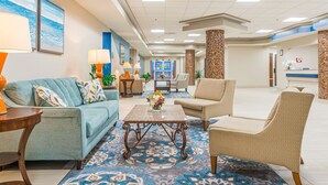 Eine Hotelhalle mit einem blauen Sofa, beigen Sesseln, einem Couchtisch mit Blumen und einem gemusterten Teppich.