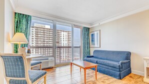 Ein Wohnzimmer mit einem blauen Sofa, einem Holztisch, einem Sessel und Blick auf ein Hochhaus durch ein großes Fenster.