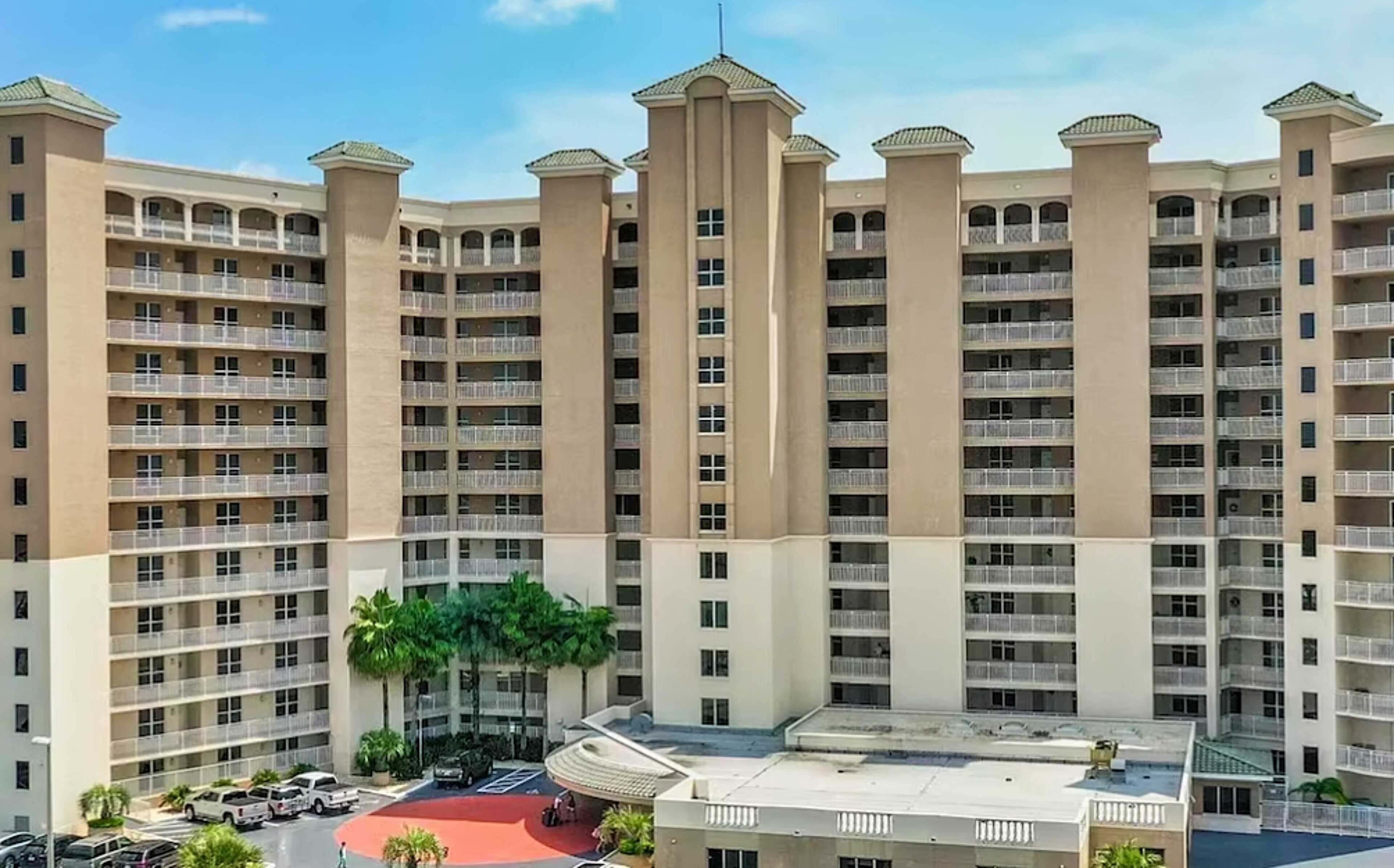 Un hôtel de grande hauteur doté de nombreux balcons, d’un parking et d’une cour intérieure agrémentée de palmiers.