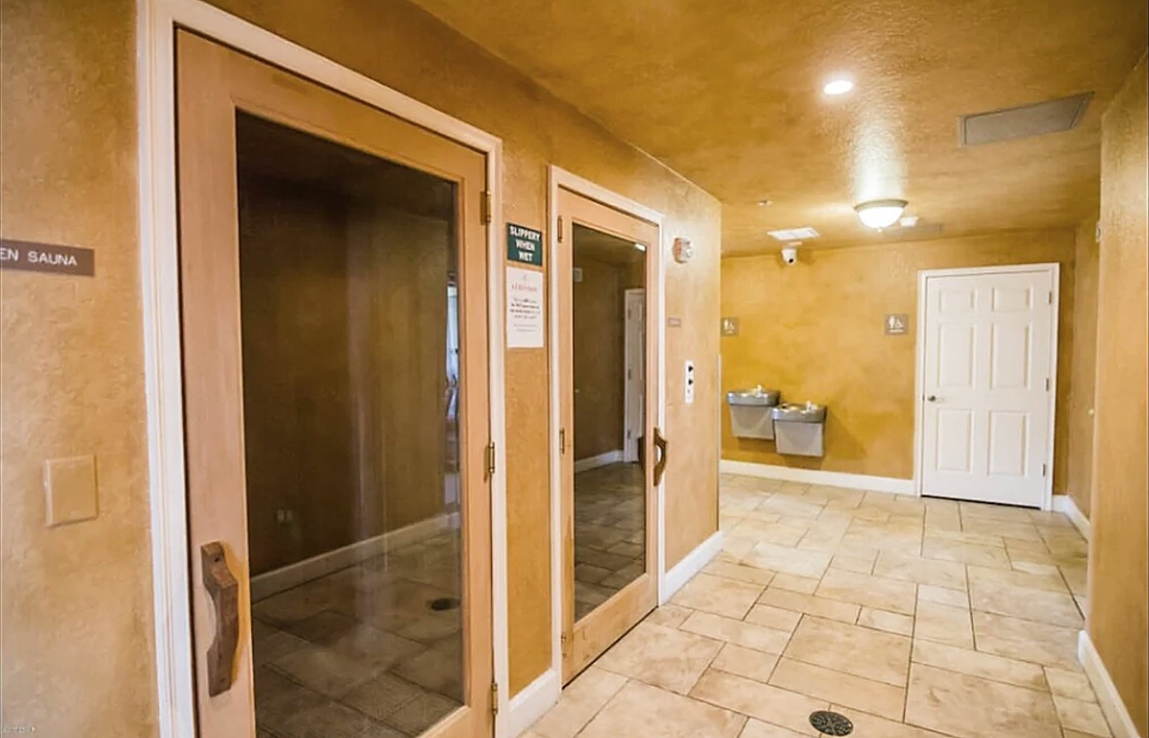 A hallway with a sauna sign, a door with a sign, and a trash bin.