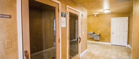 A hallway with a sauna sign, a door with a sign, and a trash bin.