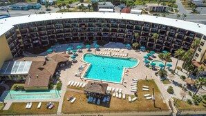 A hotel with a large pool, multiple lounge areas, and a central building with balconies.