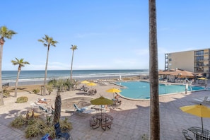 A pool area with lounge chairs and umbrellas, a beach view, and a building with balconies. - Oceanfront Studio w/ Sunrise Balcony, Pool & Beach Access (Daytona Beach Shores)