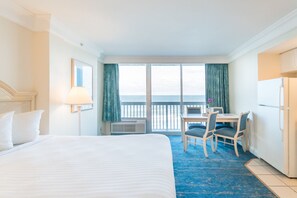Hotellihuone, jossa on suuri sänky, työpöytä ja kaksi tuolia, merinäköala ja parveke.