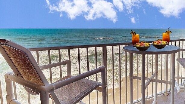 Ein Balkon mit Blick auf das Meer, ein Stuhl und ein Tisch mit Obst und Getränken.