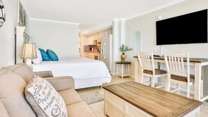 Ein Hotelzimmer mit Bett, einer Sitzecke, einem Holztisch, einem Fernseher und einer kleinen Küche im Hintergrund.